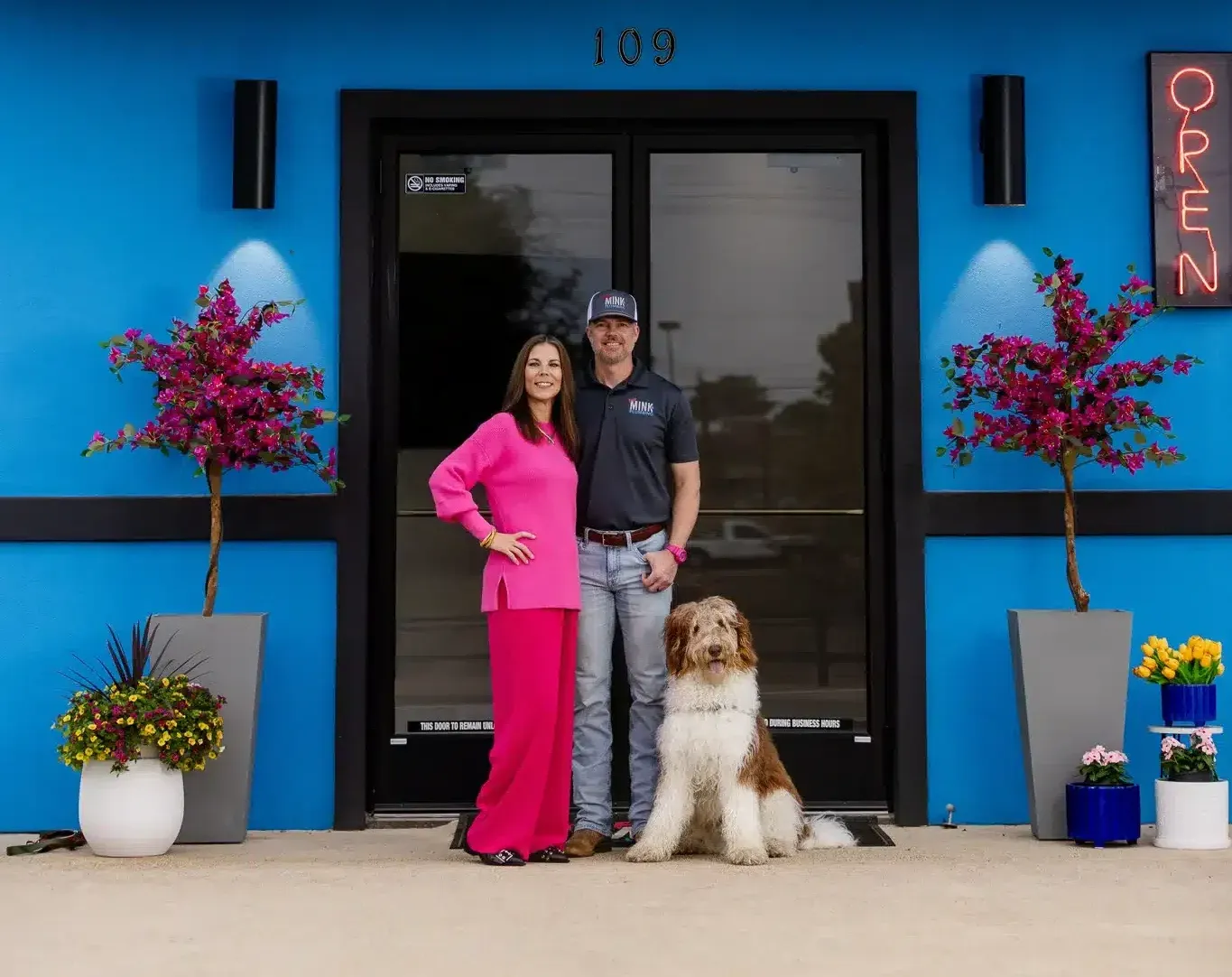 glenn and amber and dog in front of blue Mink building